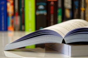 Open book lying on a white table and colorful books in a row in background